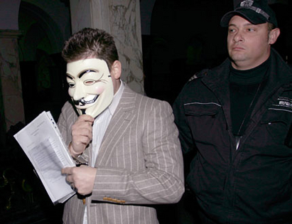 Кела влиза в съда с маска на Вендета, използвана от Анонимните